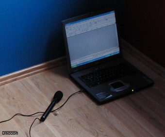 Aufgeklapptes Notebook am Boden mit linksseitig angeschlossenem, schwarzem Kondensator-Mikrofon, Audacity ist auf dessen 15-Zoll-Bildschirm ersichtlich.